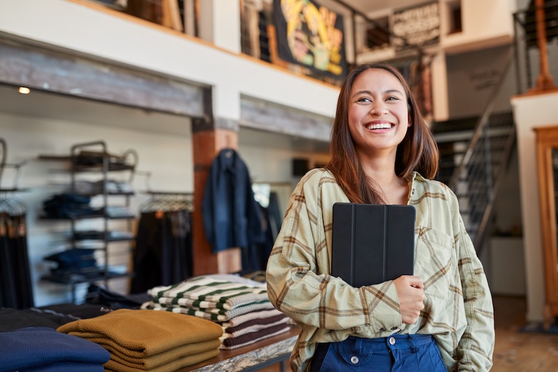 Smiling retail business owner holding a tablet in a clothing store